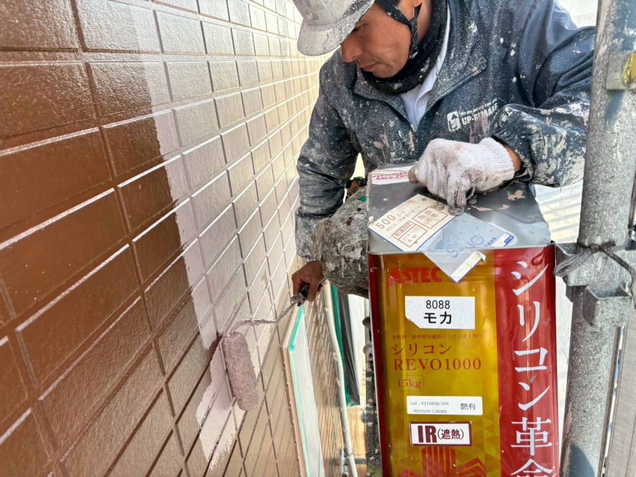 サイディング外壁に茶色の中塗り塗料をローラー施工する様子