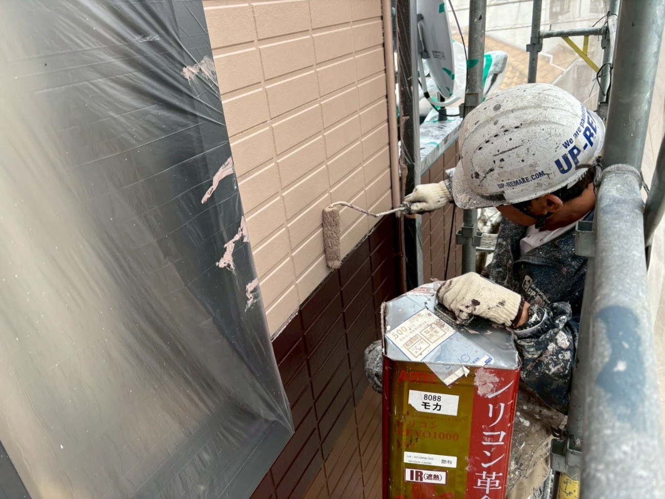 住宅脇の狭い通路でサイディング外壁をローラー塗装する職人