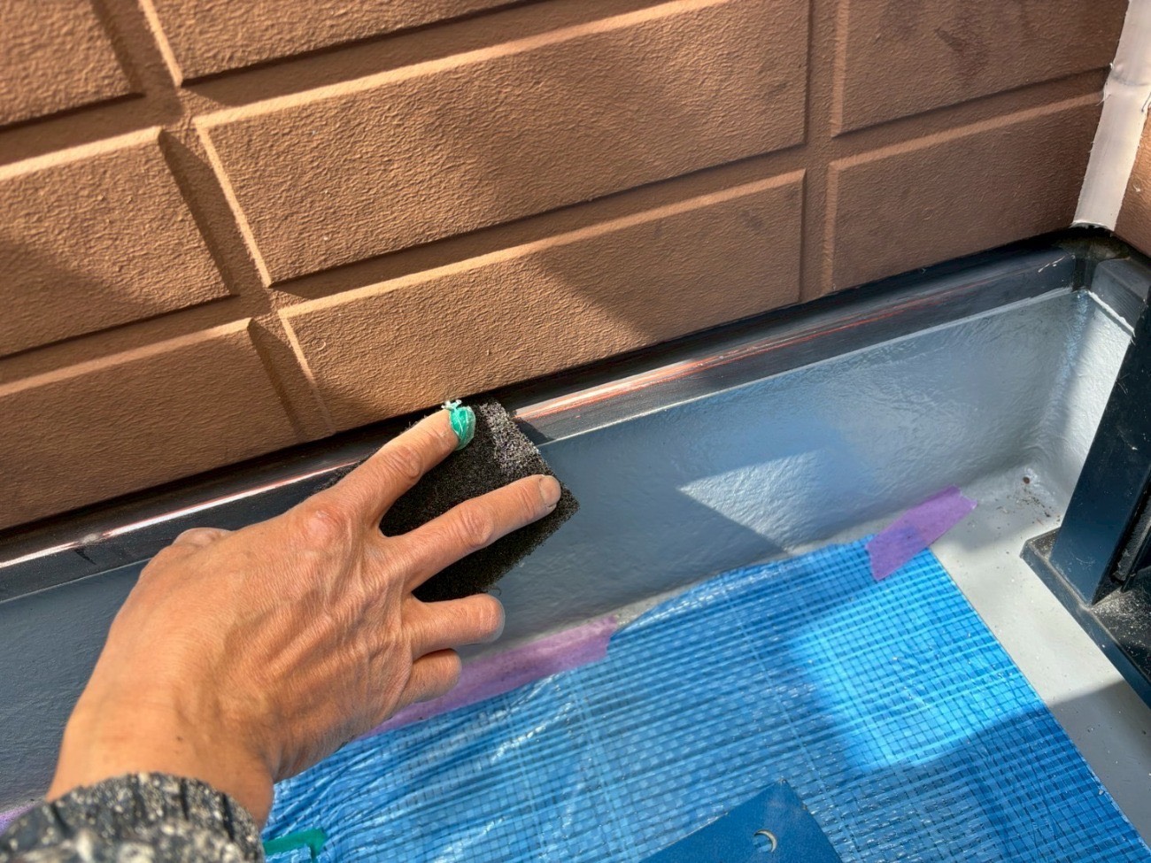 窓上の庇にグレーの錆止め塗料を施工する様子
