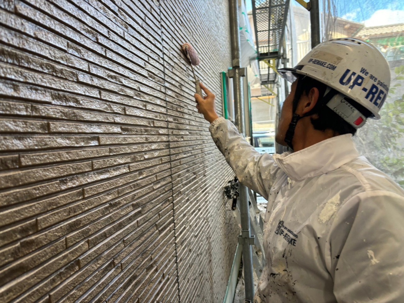 茶色いレンガ調外壁の広い範囲に塗料をローラーで塗布している様子