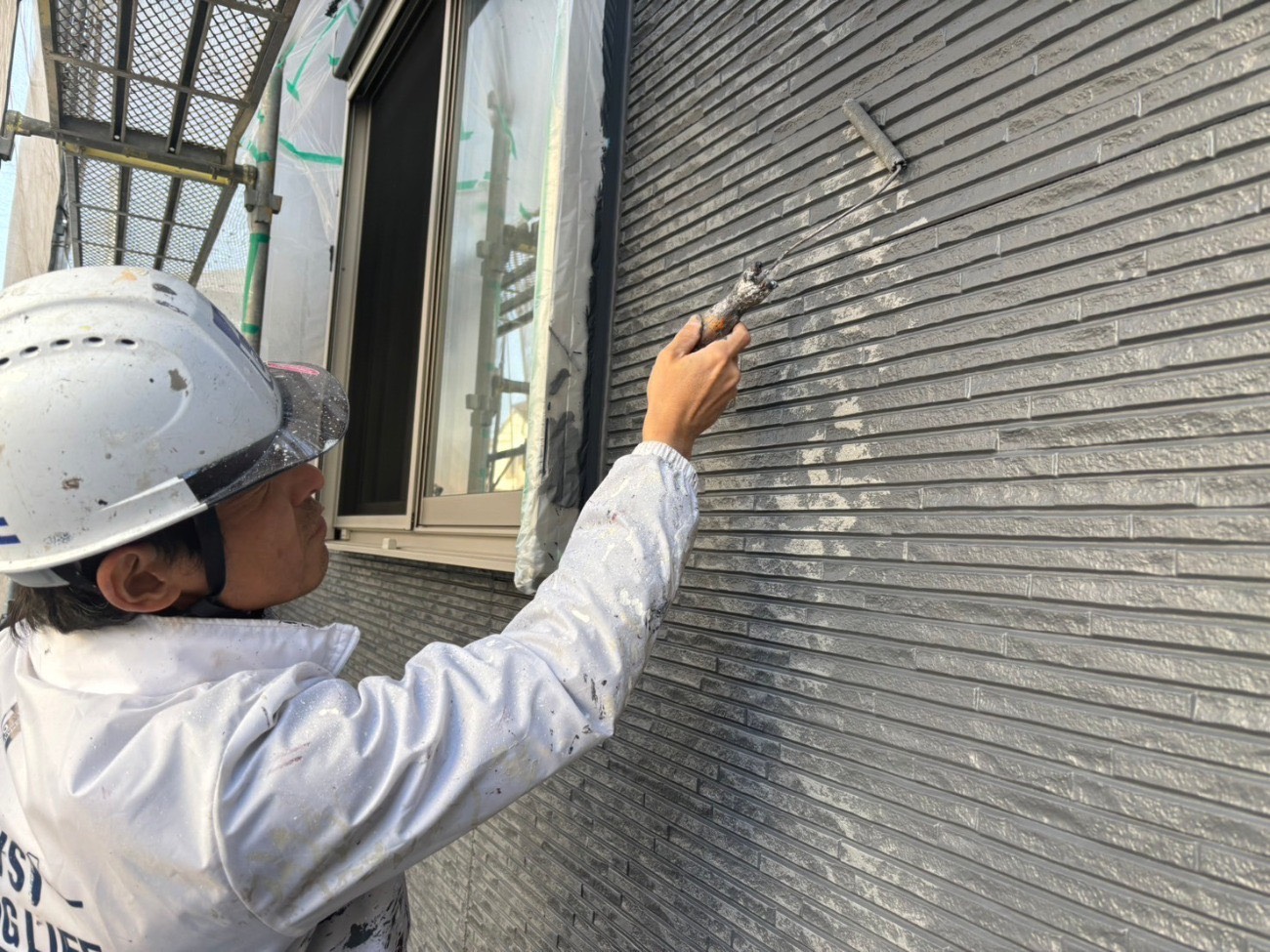 外壁にダークグレーの塗料をローラーで塗布している様子
