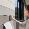 グレー系の色見本を持った女性が、建物の外壁に手を触れて色合いや質感を確認している