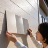 屋外で女性が明るさの異なる3色の見本板を住宅の外壁に当てて比較している