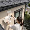 足場に立つ女性が、住宅のベージュ色の外壁に複数の色見本を当てて比較している
