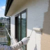 ヘルメットと手袋を着けた作業員が、足場からローラーで住宅の外壁を白く塗っている