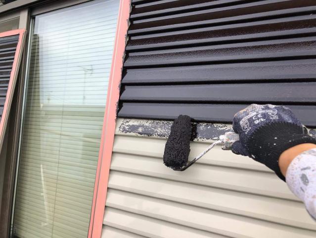 白く色あせた雨戸に黒い錆止めを塗っています